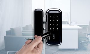 Mão aproximando chaveiro Intelbras de fechadura eletrônica com teclado numérico instalada em porta de vidro de escritório