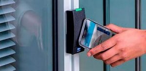 Pessoa aproximando o celular de leitor de controle de acesso instalado em porta de vidro para liberação por credencial móvel