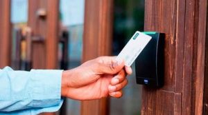 Mão aproximando cartão de proximidade branco de leitor instalado em portão de madeira