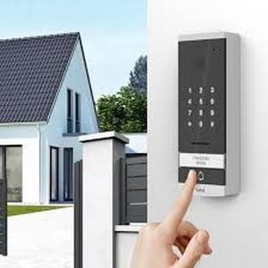 Pessoa digitando senha em fechadura com teclado digital instalada em portão residencial, com casa ao fundo