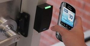 Pessoa aproximando o celular com aplicativo HID de leitor de proximidade instalado ao lado de porta com fechadura