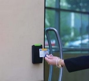 Mão aproximando cartão de proximidade de leitor instalado em porta de vidro