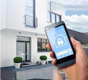 Mão segurando smartphone com aplicativo de controle de acesso de uma casa ao fundo