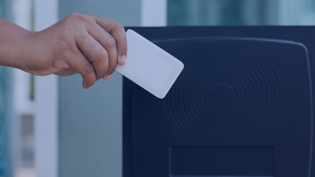 Mão aproximando cartão RFID branco de leitora escura instalada em porta de vidro